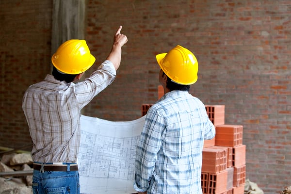 Architects at a construction site looking at blueprints and pointing