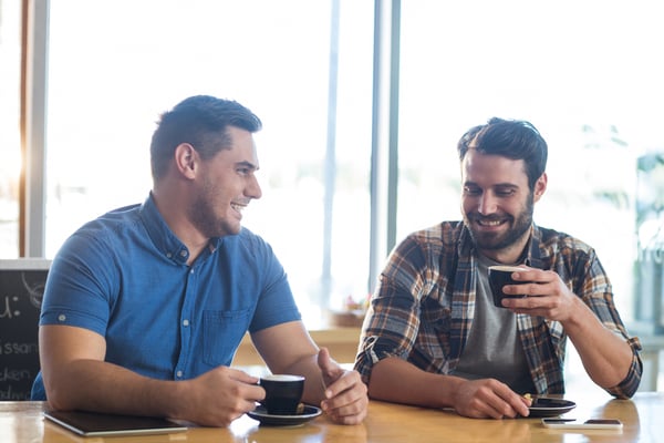 Male friends interacting while having a cup of coffee in cafx92xA9