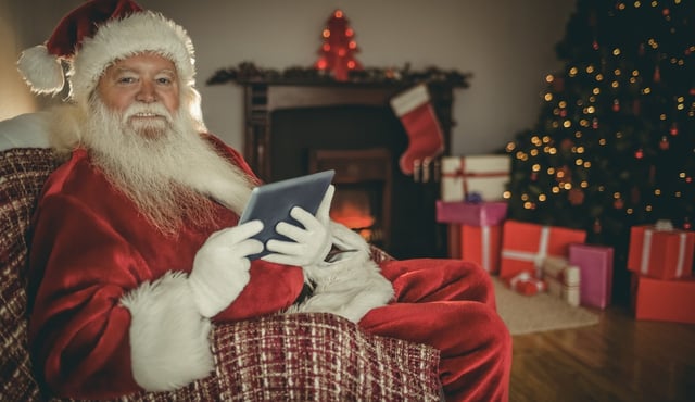 Cheerful santa using tablet on the couch at home in the living room.jpeg
