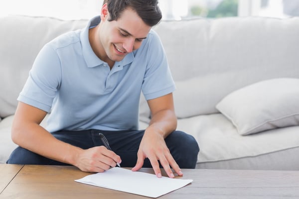 Man writing on a paper while he is sat on a couch