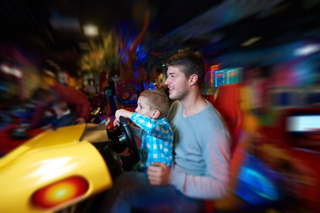 happy father and son playing driving wheel video game in playground theme park.jpeg